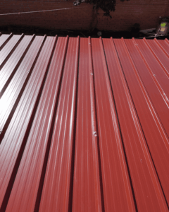 Detalle de cubierta de panel sándwich 5 grecas color rojo teja instalada en porche residencial en Tarragona