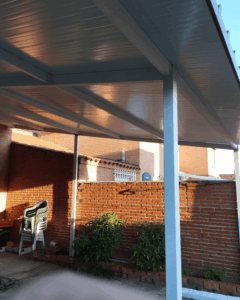 Vista interior de porche residencial con cubierta de panel sándwich 5 grecas sobre estructura metálica